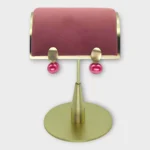 A pair of Auralis Drop earrings with pink pearls displayed on a gold stand.