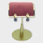 A pair of Auralis Drop earrings with gold oval studs and dark spherical drops on a gold display stand.