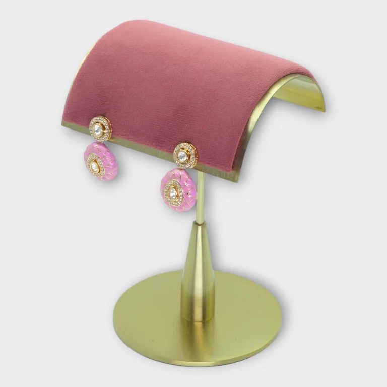 Drop pearl earrings with pink and gold accents displayed on a modern gold stand for MEENA product page.