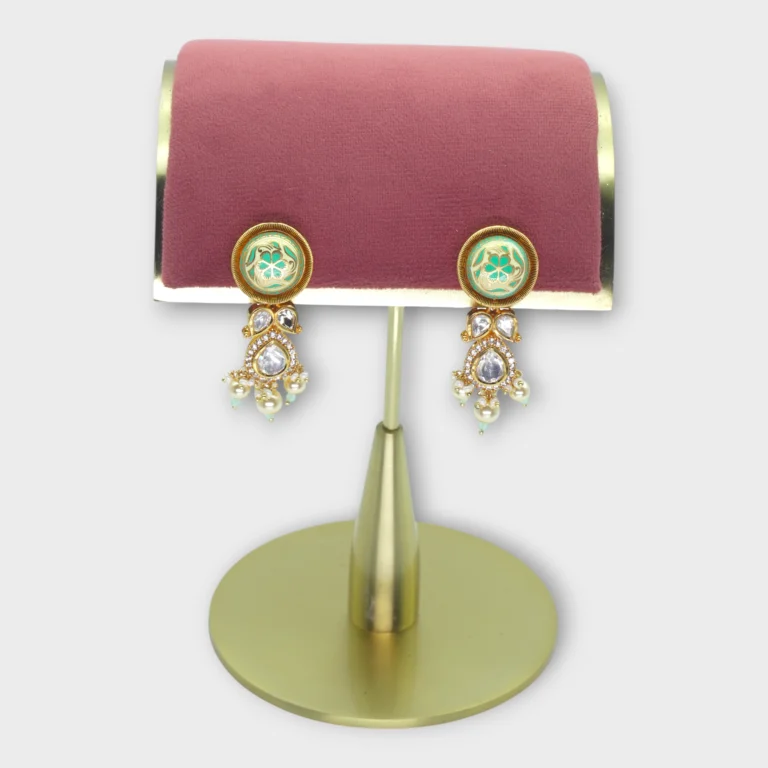 Elegant pearl earrings for bride with green accents and gold detailing displayed on a pink and gold stand.