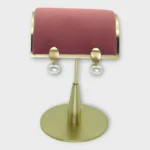 A pair of Auralis Drop pearl earrings displayed on a gold stand with a pink cushion.