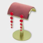 Riva Cascade gold and red drop earrings displayed on a pink and gold jewelry stand.