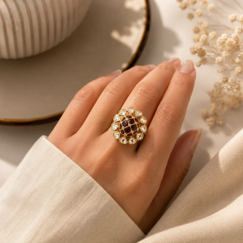 Women wearing STONIRA gold cocktail ring featuring a central glossy crimson red domed stone with a gold grid overlay and an outer halo of clear teardrop gems