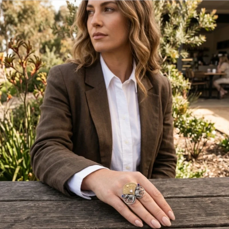 Women wearing STONIRA adjustable mixed-metal cocktail ring featuring oxidized silver elephants, a golden archway, and sapphire crystal accents