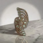 Women wearing STONIRA adjustable gold cocktail ring with a mint green stone floral rosette and crystal-paved arches