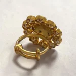 Back view of STONIRA gold cocktail ring featuring a central glossy crimson red domed stone with a gold grid overlay and an outer halo of clear teardrop gems