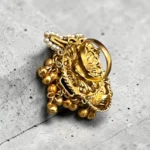 Back view of STONIRA adjustable gold temple charm ring featuring red gemstone, pearl accents, intricate heritage motifs and ghungroo detailing for festive and wedding wear.