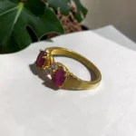 Angle-view-of-STONIRA-gold-plated-statement-ring-featuring-a-balanced-vertical-alignment-of-two-oval-ruby-pink-gemstones-connected-by-a-delicate-S-curve-of-clear-crystal-pave