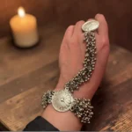 Close up of STONIRA oxidised silver floral hathphool hand harness bracelet featuring sunburst medallions and dense ghungroo bell clusters