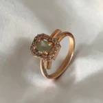 Close-up-of-the-STONIRA-rose-polished-sage-green-statement-ring-worn-on-a-hand-highlighting-the-soft-green-hue-and-sparkling-crystal-halo-against-warm-linen-fabric.