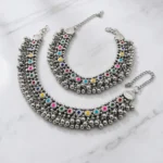 STONIRA-broad-oxidized-silver-payal-set-featuring-colorful-stone-cabochons-and-dense-dangling-ghungroo-bells-on-a-marble-background