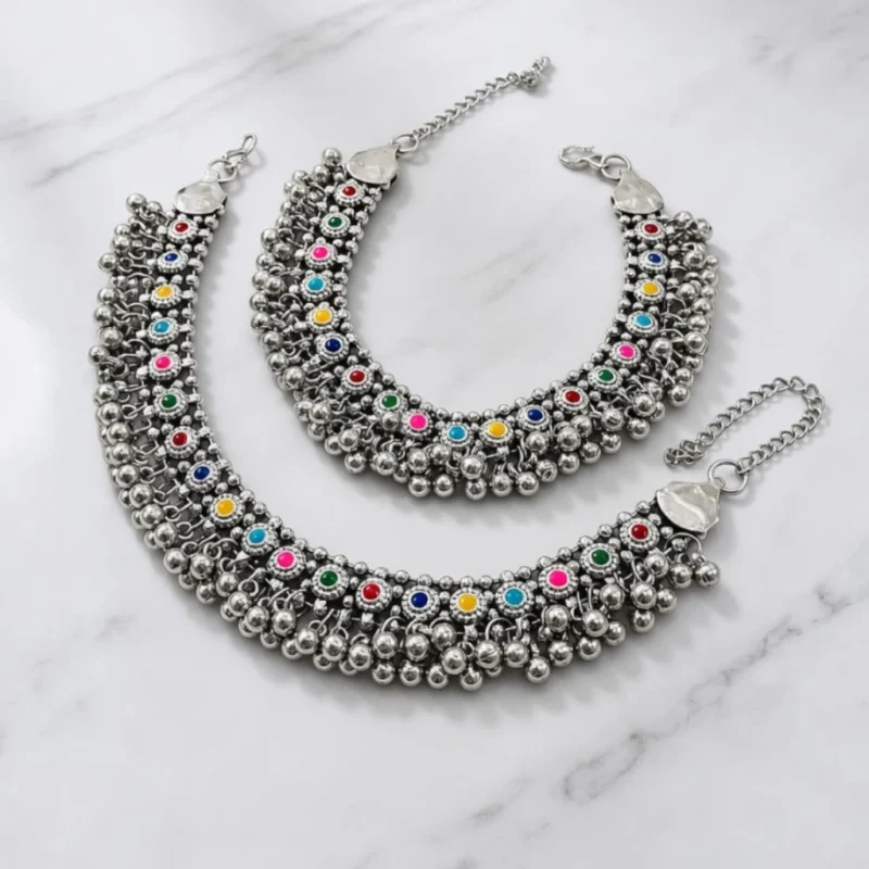 STONIRA-broad-oxidized-silver-payal-set-featuring-colorful-stone-cabochons-and-dense-dangling-ghungroo-bells-on-a-marble-background