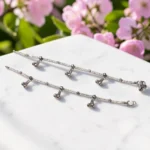 STONIRA-handcrafted-pair-of-oxidized-silver-anklets-with-multicolor-enamel-flowers-and-ghungroo-charms-laid-on-white-marble-with-flowers