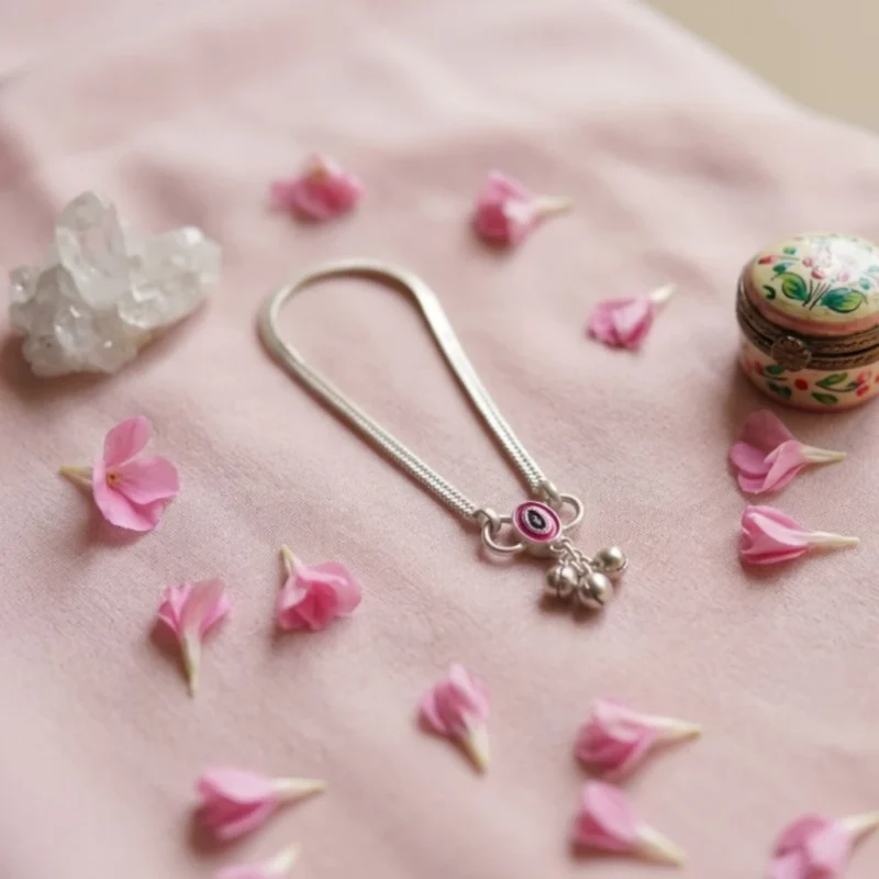 STONIRA-modern-silver-snake-chain-payal-anklet-arranged-on-a-soft-pink-cloth-backdrop-surrounded-by-scattered-pink-petals-a-quartz-crystal-and-a-small-trinket-box.