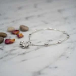STONIRA-modern-silver-snake-chain-payal-anklet-with-cylindrical-beads-laid-flat-on-a-polished-white-marble-surface-next-to-dried-flower-petals-and-smooth-river-stones