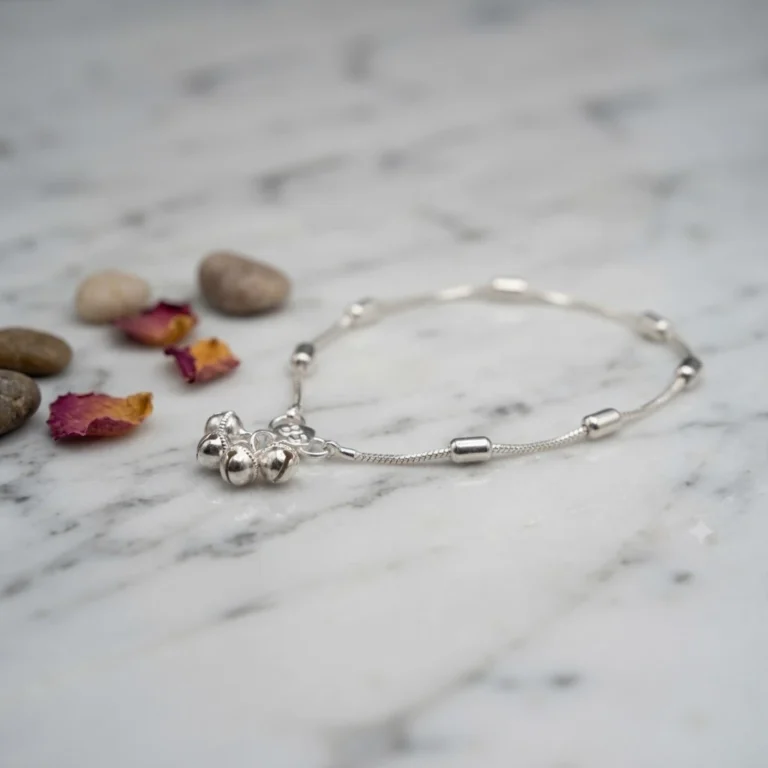 STONIRA-modern-silver-snake-chain-payal-anklet-with-cylindrical-beads-laid-flat-on-a-polished-white-marble-surface-next-to-dried-flower-petals-and-smooth-river-stones