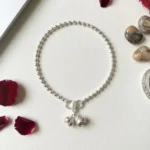 STONIRA-modern-silver-spherical-bead-payal-anklet-laid-in-a-neat-circle-on-textured-cream-paper-alongside-deep-red-rose-petals-and-smooth-river-stones