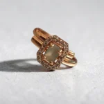 STONIRA-rose-polish-statement-ring-featuring-a-rectangular-sage-green-gemstone-enclosed-in-an-octagonal-halo-of-shimmering-clear-crystals-on-a-neutral-backdrop