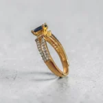 Side view of STONIRA gold-plated adjustable ring showcasing the overlapping custom-fit band, clear micro-crystal accents, and elevated navy blue gemstone basket setting.