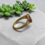 Side-view-of-STONIRA-gold-plated-statement-ring-featuring-a-balanced-vertical-alignment-of-two-oval-ruby-pink-gemstones-connected-by-a-delicate-S-curve-of-clear-crystal-pave.