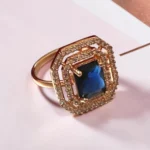 Side-view-of-the-STONIRA-rose-gold-polished-navy-blue-statement-ring-worn-on-a-hand-highlighting-the-deep-blue-rectangular-gemstone-and-double-crystal-halo
