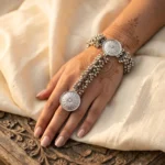 Women wearing STONIRA oxidised silver floral hathphool hand harness bracelet featuring sunburst medallions and dense ghungroo bell clusters
