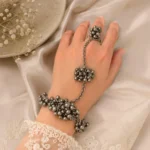 Women wearing STONIRA oxidised silver ghungroo haathphool hand harness bracelet featuring bead cluster embellishments and adjustable finger ring