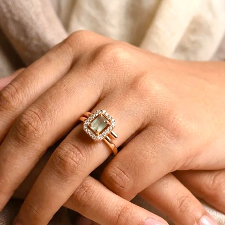 Women-wearing-STONIRA-rose-polish-statement-ring-featuring-a-rectangular-sage-green-gemstone-enclosed-in-an-octagonal-halo-of-shimmering-clear-crystals-on-a-neutral-backdrop
