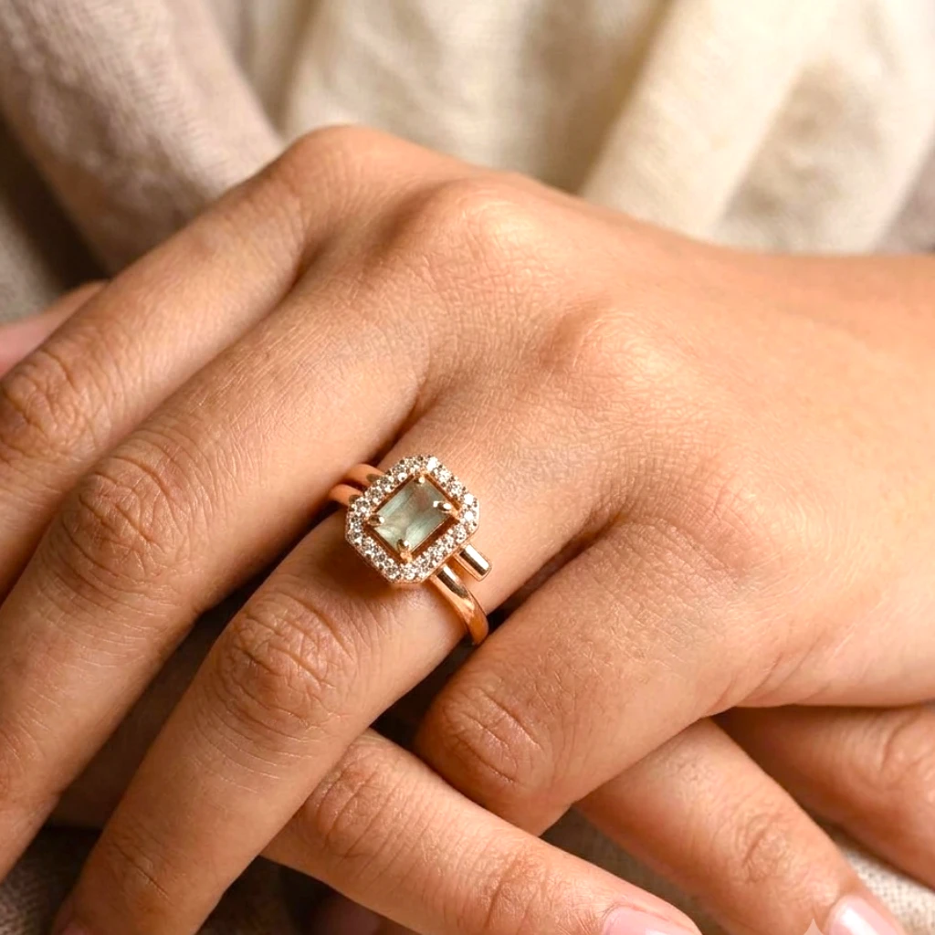 Women wearing STONIRA rose-polish statement ring featuring a rectangular sage-green gemstone enclosed in an octagonal halo of shimmering clear crystals on a neutral backdrop Women-wearing-STONIRA-rose-polish-statement-ring-featuring-a-rectangular-sage-green-gemstone-enclosed-in-an-octagonal-halo-of-shimmering-clear-crystals-on-a-neutral-backdrop