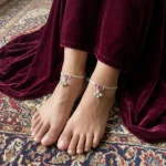 Women-wearing-STONIRA-silver-payal-anklet-on-a-foot-highlighting-the-pink-enamel-charm-and-three-small-hanging-silver-bells.