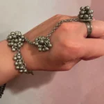 Women wearing in hand STONIRA oxidised silver ghungroo haathphool hand harness bracelet featuring bead cluster embellishments and adjustable finger ring