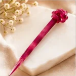 Berry magenta translucent resin hair stick with a sculpted knot detail resting on a marble surface