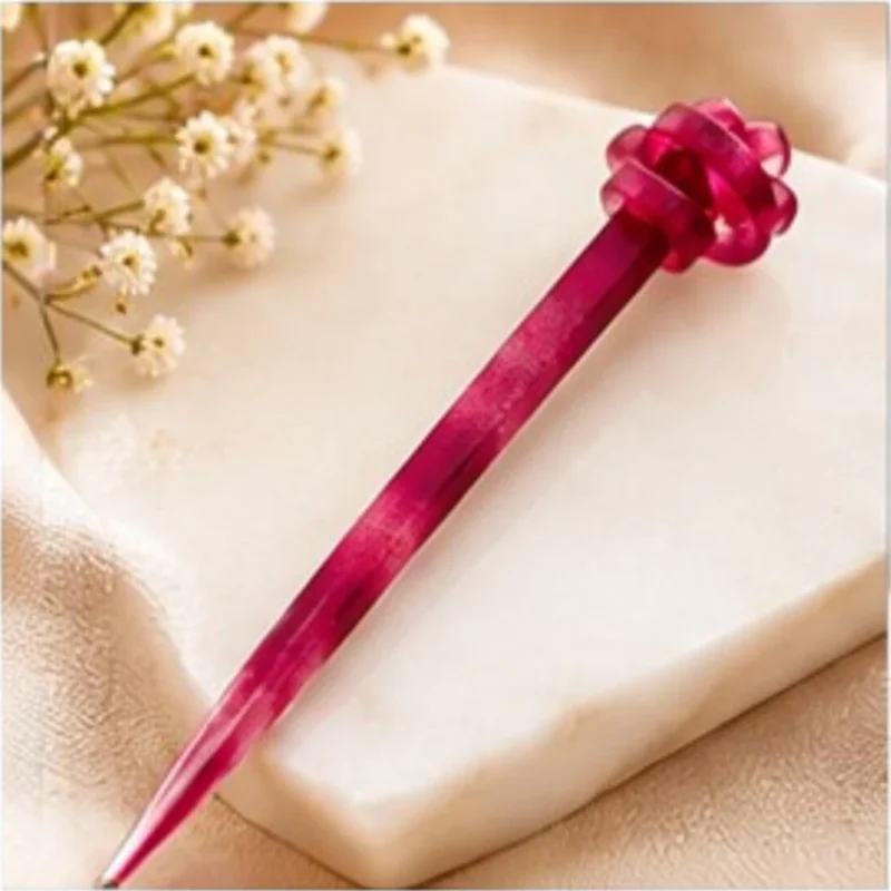 Berry magenta translucent resin hair stick with a sculpted knot detail resting on a marble surface