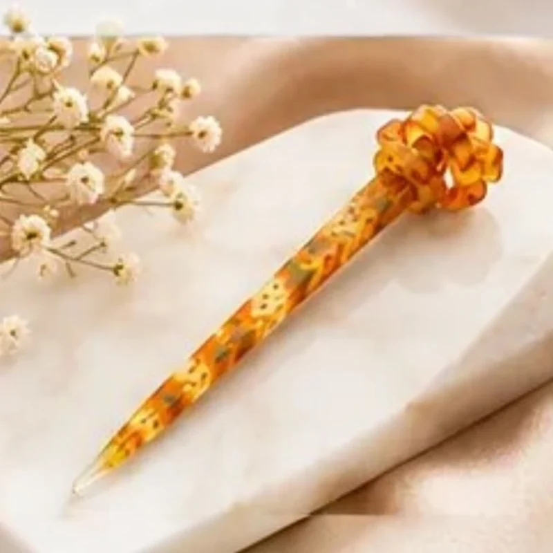 Warm amber mustard resin hair stick with an intricate floral pattern and sculpted knot top